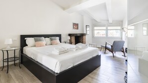 Une chambre moderne avec un grand lit, une cheminée, un fauteuil et une petite table.