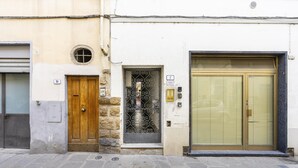 Un bâtiment avec une porte en bois, une fenêtre dotée d’une grille métallique et une porte de volet fermée.