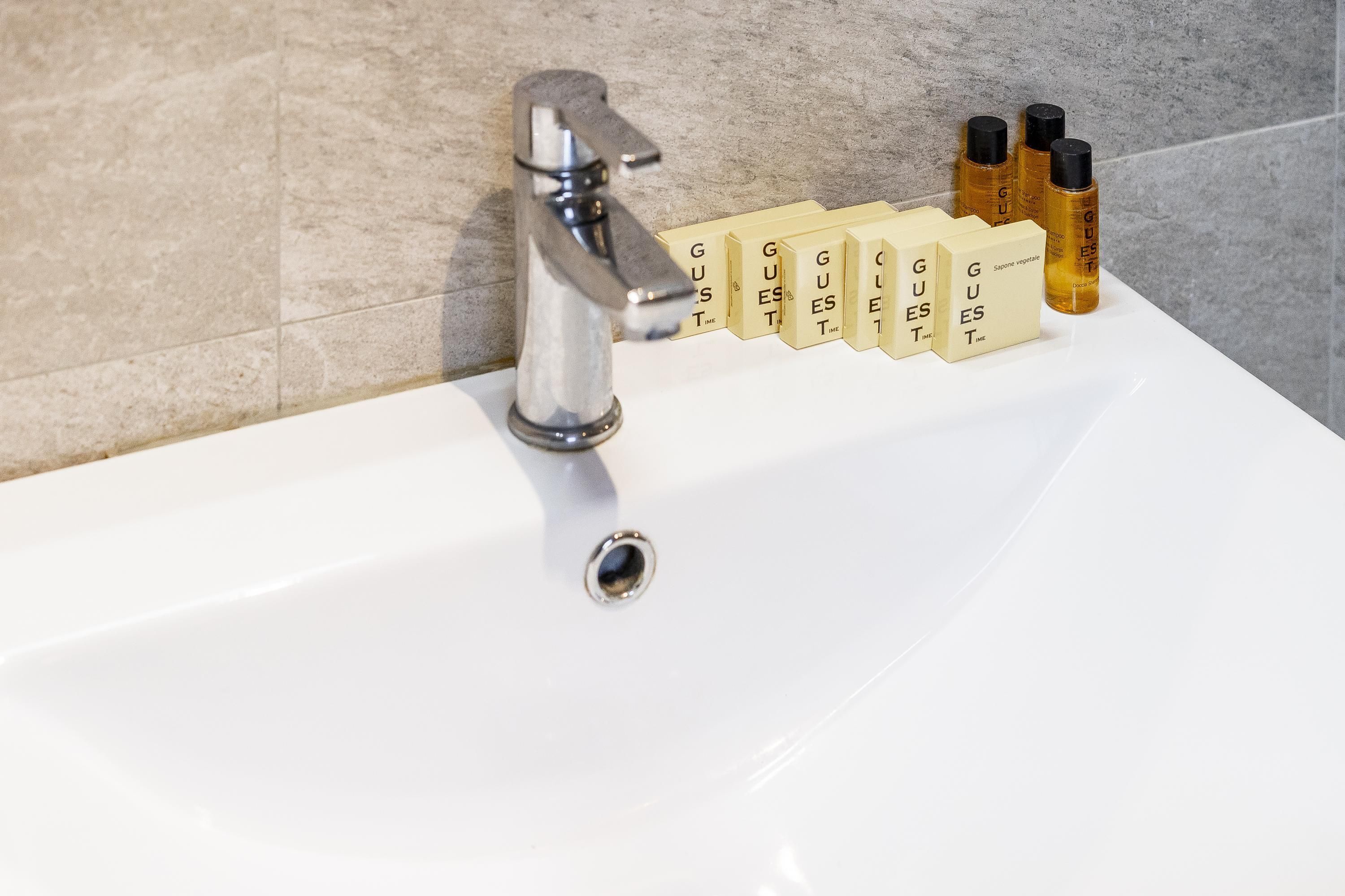 Ein Badezimmerwaschbecken mit chromfarbenem Wasserhahn und einer Reihe von Pflegeprodukten mit der Aufschrift „GUEST“.