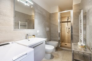A modern bathroom with a white vanity, a toilet, a shower with a glass door, and a mirror with lights.