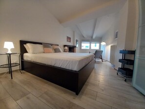A modern bedroom with a large bed, a bedside table with a lamp, a chair, and a small table with a lamp.