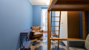 Een kamer met een blauwe wand, een gestreept sofa, een houten ladder en een grijze fauteuil.