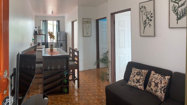A modern living room with a black sofa and floral cushions, a dining area with a wooden table and chairs, and a kitchen in the background. - coati del arenal (La Fortuna)