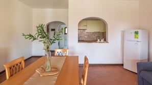 A dining area with a wooden table, chairs, and a vase with green plants. There is a kitchen visible through an archway in the background. - Charming Small Villa Bella villetta no2020 (Stintino)