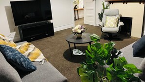 A living room with a flat-screen TV, a sofa, a chair, a coffee table, and a potted plant. - Luxurious House Next to St Clair Beach (Dunedin)