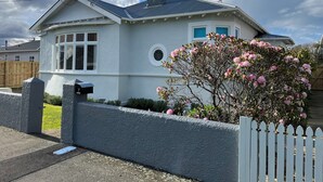 A house with a white exterior, a grey roof, and a small garden with pink flowers. - Luxurious House Next to St Clair Beach (Dunedin)