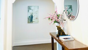 A hallway with a white ceiling, a yellow light fixture, a wooden table with a vase of flowers, and a mirror on the wall. - Luxurious House Next to St Clair Beach (Dunedin)