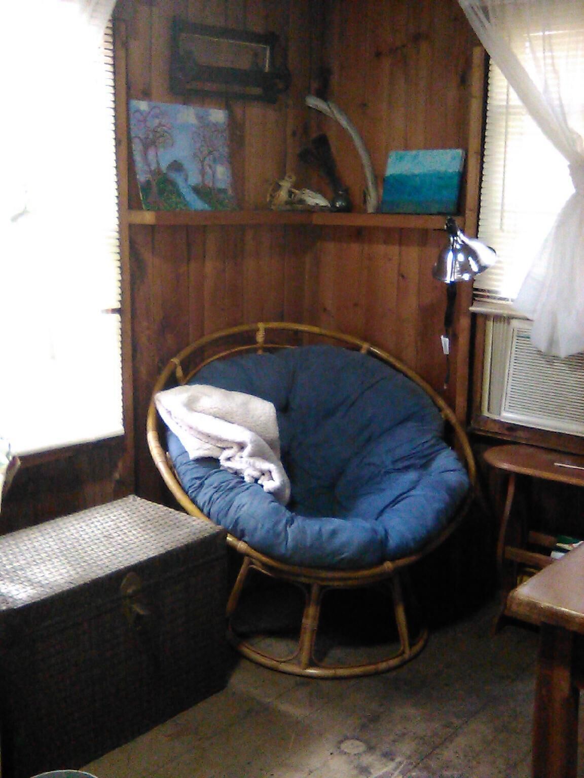 A room with a wicker rocking chair, a small table, and a window with curtains.