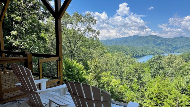 Ein überdachter Außenbereich mit Adirondack-Stühlen mit Blick auf eine Berglandschaft und einen See.