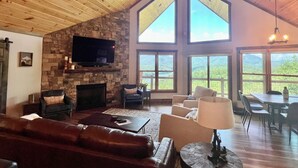 Ein geräumiges Wohnzimmer mit Kamin aus Stein, einer Ledersofa und einem großen, an der Wand befestigten Fernseher.