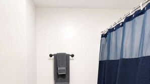 A small bathroom with a toilet, a towel rack, a shower curtain, a floor mat, and a trash bin. - Stand Rock Studios in Wisconsin Dells! (Wisconsin Dells)