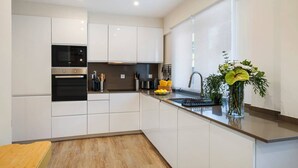 A modern kitchen with white cabinetry, stainless steel appliances, and a wooden floor. - Monte Estoril Seabreeze by Portugal Portfolio (Estoril)