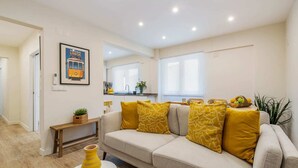 A modern living room with a beige sofa, yellow cushions, a small coffee table with books and a vase, and a framed picture on the wall. - Monte Estoril Seabreeze by Portugal Portfolio (Estoril)
