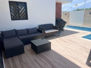 Une terrasse avec un canapé, une petite table et un barbecue abrité.