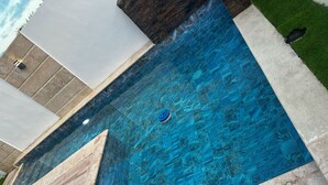 Une piscine à l’eau d’un bleu cristallin, entourée de carreaux de pierre et bordée d’une pelouse.