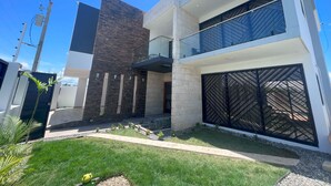 Une maison moderne à deux étages, dotée d’un toit plat, d’un balcon et d’une grande porte de garage.