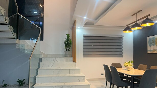 Un intérieur moderne avec un escalier, un coin repas et un luminaire fixé au mur.