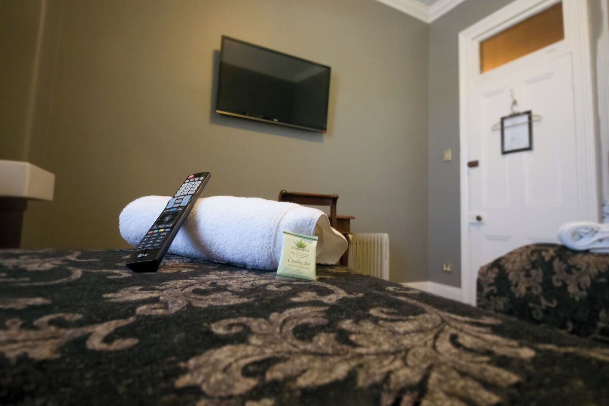 A neatly made bed with a remote control and a cleaning bar on it.