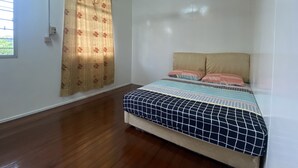 Un dormitorio con cama, ventana con cortina, unidad de aire acondicionado y piso de madera.