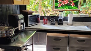 Ett kök med mikrovågsugn, kaffebryggare och mixer på bänkskivan, och utsikt över grönområden utanför.