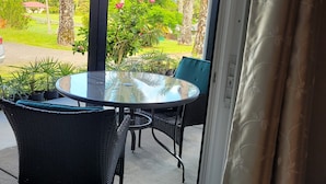 Ett takförsett utomhusområde med ett glasbord och stolar, utsikt över grönska och en byggnad i fjärran.