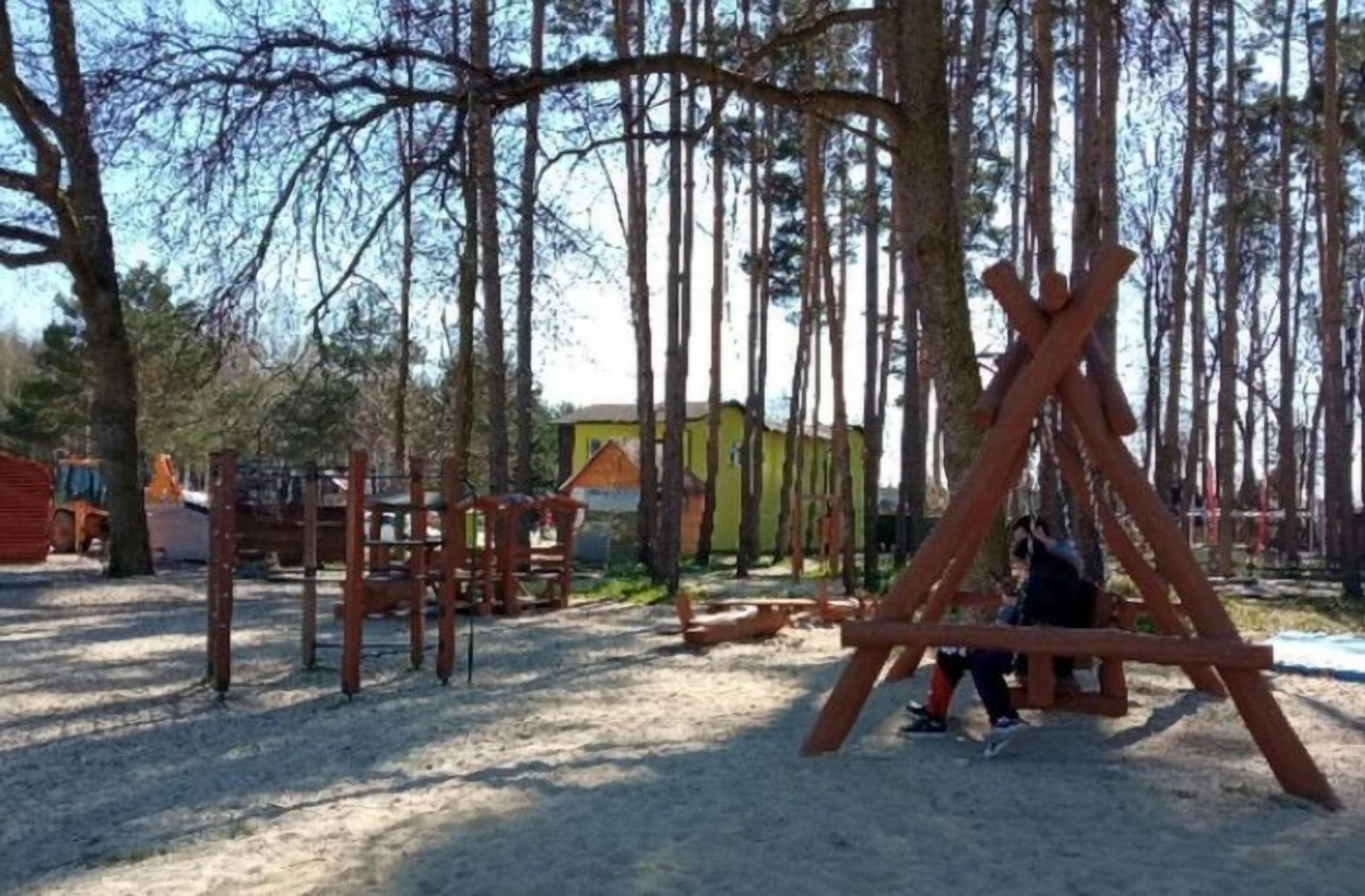 Une aire de jeux avec des balançoires et des structures d’escalade, située dans un espace boisé.