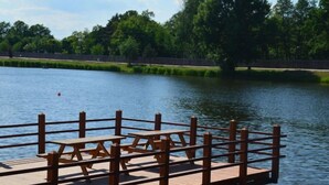 A wooden dock with picnic tables extending over a calm lake, surrounded by lush greenery and trees.