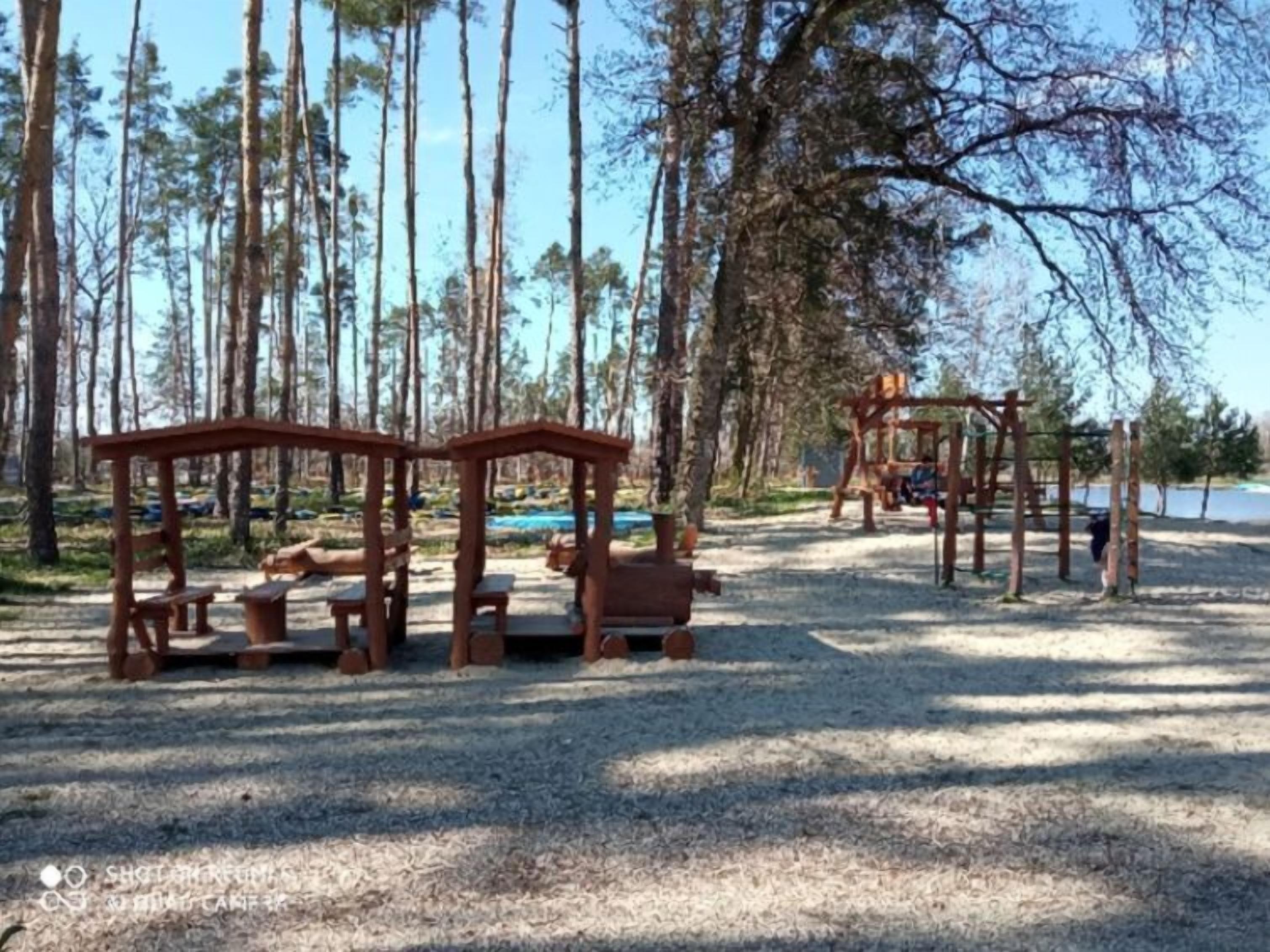 Une aire de jeux avec des structures et des bancs en bois, située dans une zone boisée.