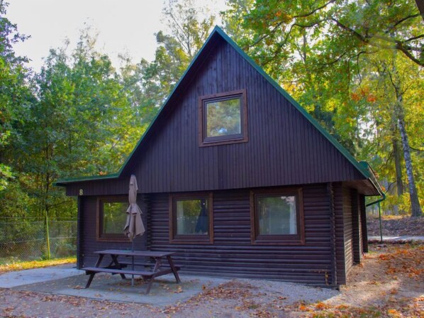 A cabin with a pitched roof, large windows, and a picnic table.