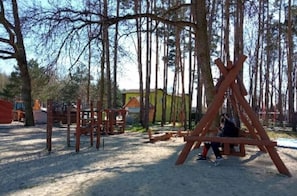 A playground with swings and climbing structures in a wooded area.