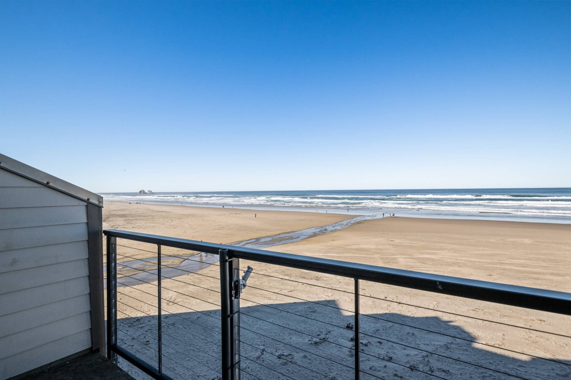 Blick vom Balkon mit Geländer auf einen Sandstrand und das Meer im Hintergrund.