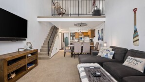 A spacious living room with a high ceiling, a staircase leading to an upper level, a dining area, and a kitchen. - Extraordinary Oceanfront Views at Rockaway Creek Inn, Patio and Living Area Bathed In Natural Light (Rockaway Beach)