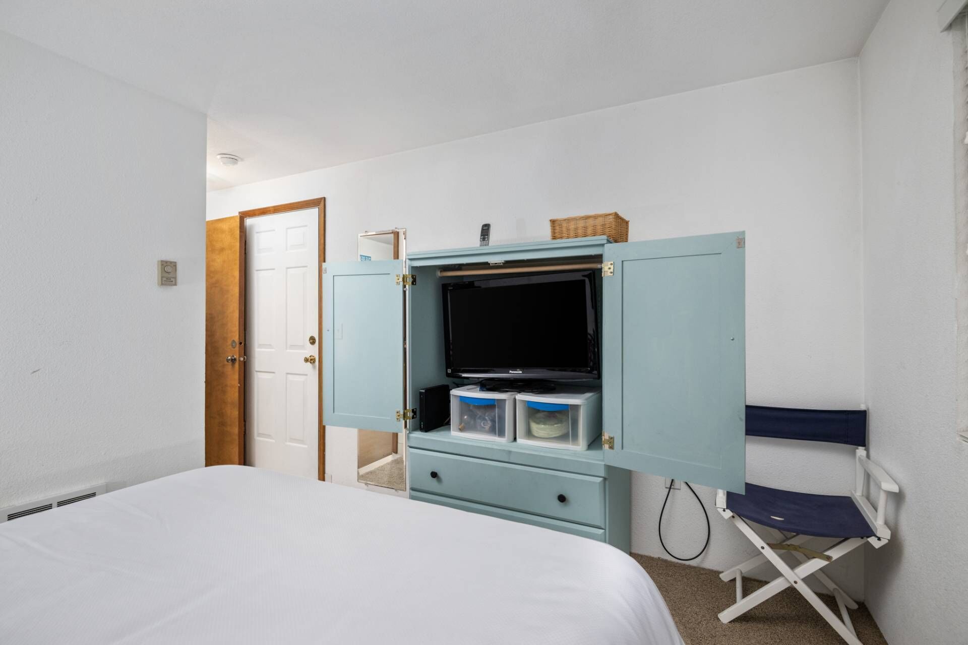 Ein Schlafzimmer mit einem Bett, einem Schrank mit Fernseher und einem Sessel.