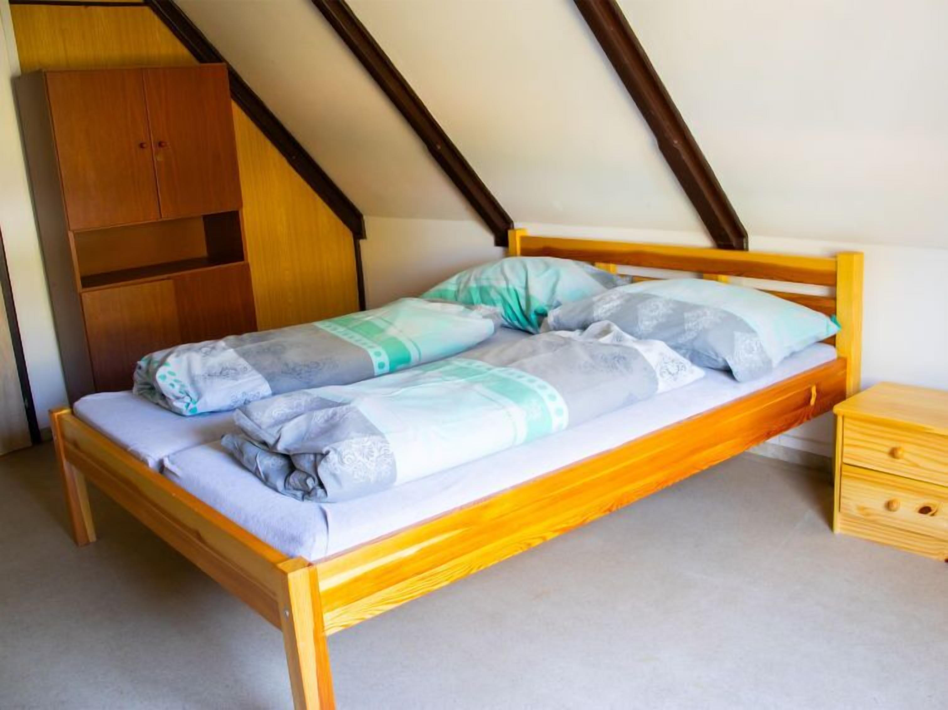 A single bed with a wooden frame and a headboard, a wooden nightstand with a drawer, and a wooden wardrobe with a small shelf.