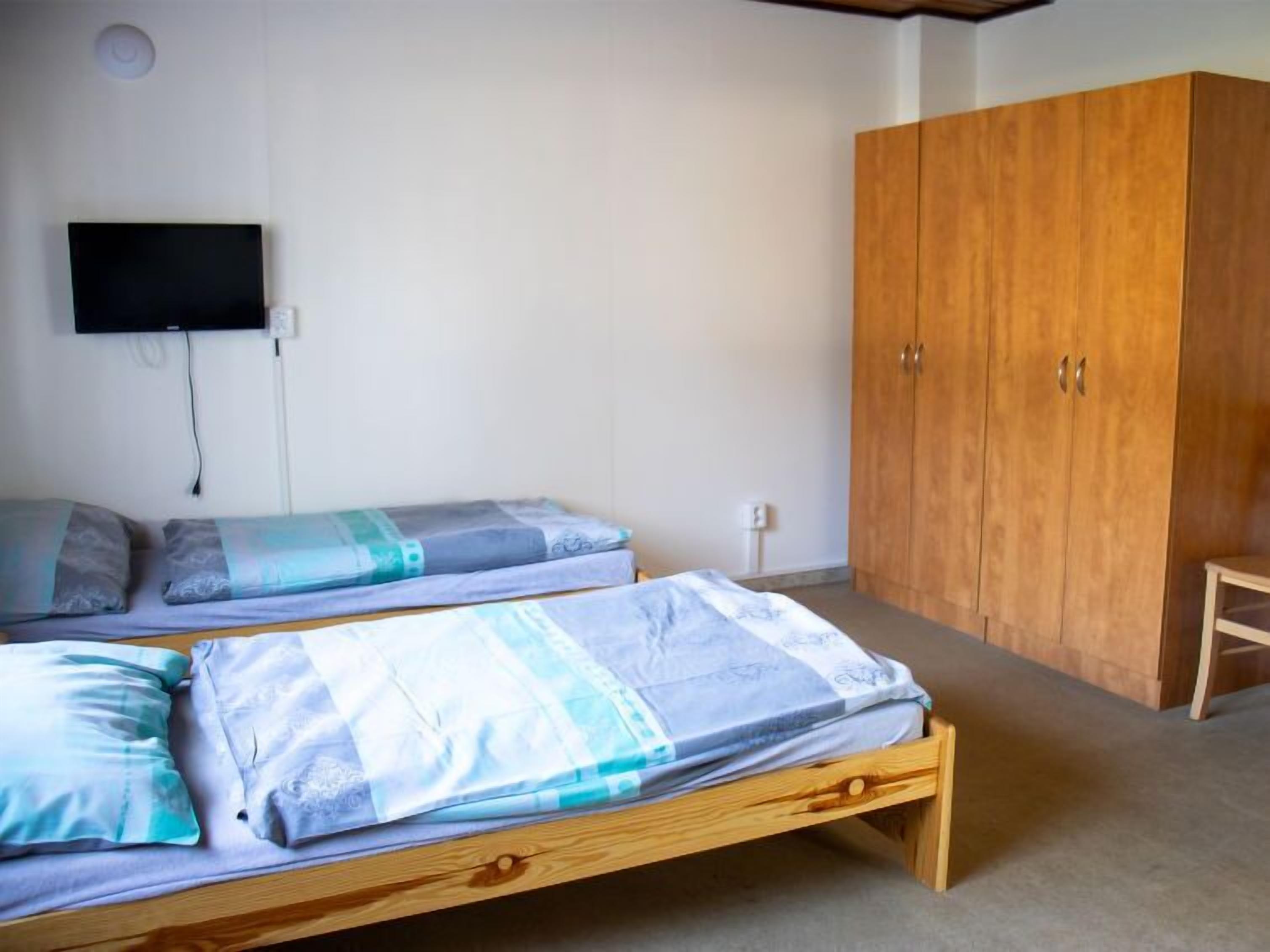 A room with two wooden beds, a wardrobe, and a television mounted on the wall.