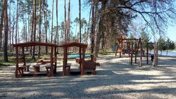 Une aire de jeux avec des structures et des bancs en bois, située dans une zone boisée.