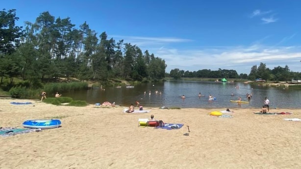 Ranta, jossa on järvi, puita sekä ihmisiä uimassa ja ottamassa aurinkoa.