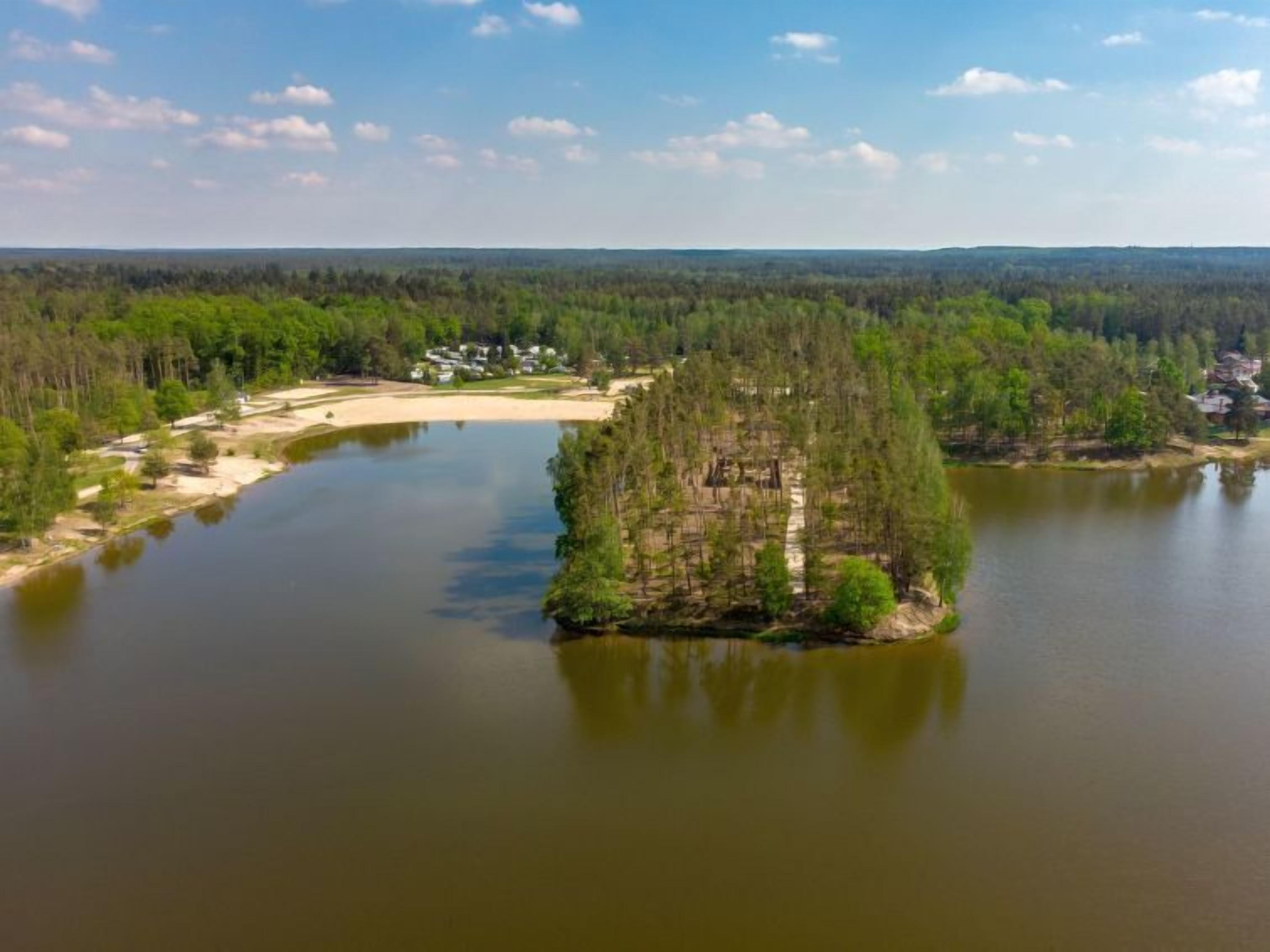 An aerial view of a lake with a small island and a residential area with houses and a sandy beach.