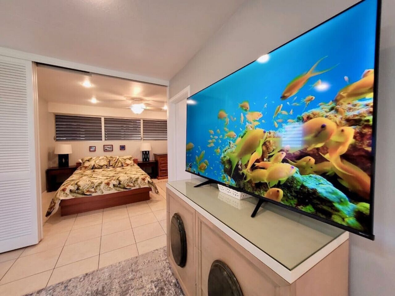 Ein Schlafzimmer mit einem Bett, einem an der Wand montierten Fernseher und einem Fenster mit Jalousien.