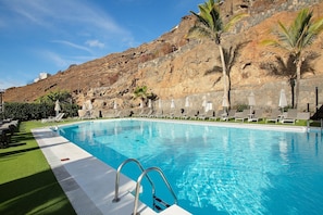 A swimming pool with a stone wall and palm trees in the background. - Zen House Holiday Home with Sea View, Communal Pool, and Wi-Fi (Puerto Rico)