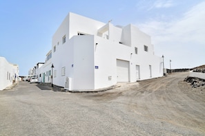 Un edificio blanco con una puerta de garaje, un camino de tierra y un cielo despejado.