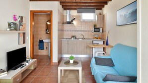 Un espace de vie compact comprenant un téléviseur, un canapé, une cuisine et des poutres en bois au plafond.