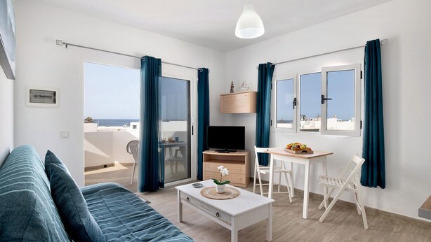 A modern living room with a sofa, a coffee table, a TV, a wooden cabinet, and a dining area with chairs.