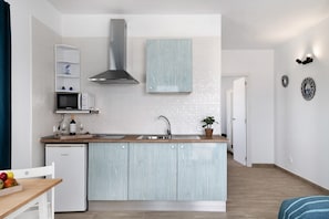 A compact kitchen with a microwave, a built-in oven, a stainless steel range hood, a sink, and a light blue cabinet.