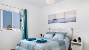 A bedroom with a bed, a nightstand, a window with curtains, and a wall-mounted painting.