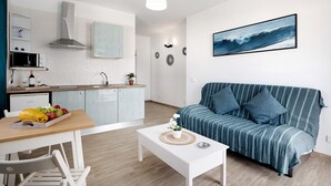 A modern kitchen with a microwave, sink, and cabinets, a dining table with fruit, a white sofa, and a wall-mounted picture.