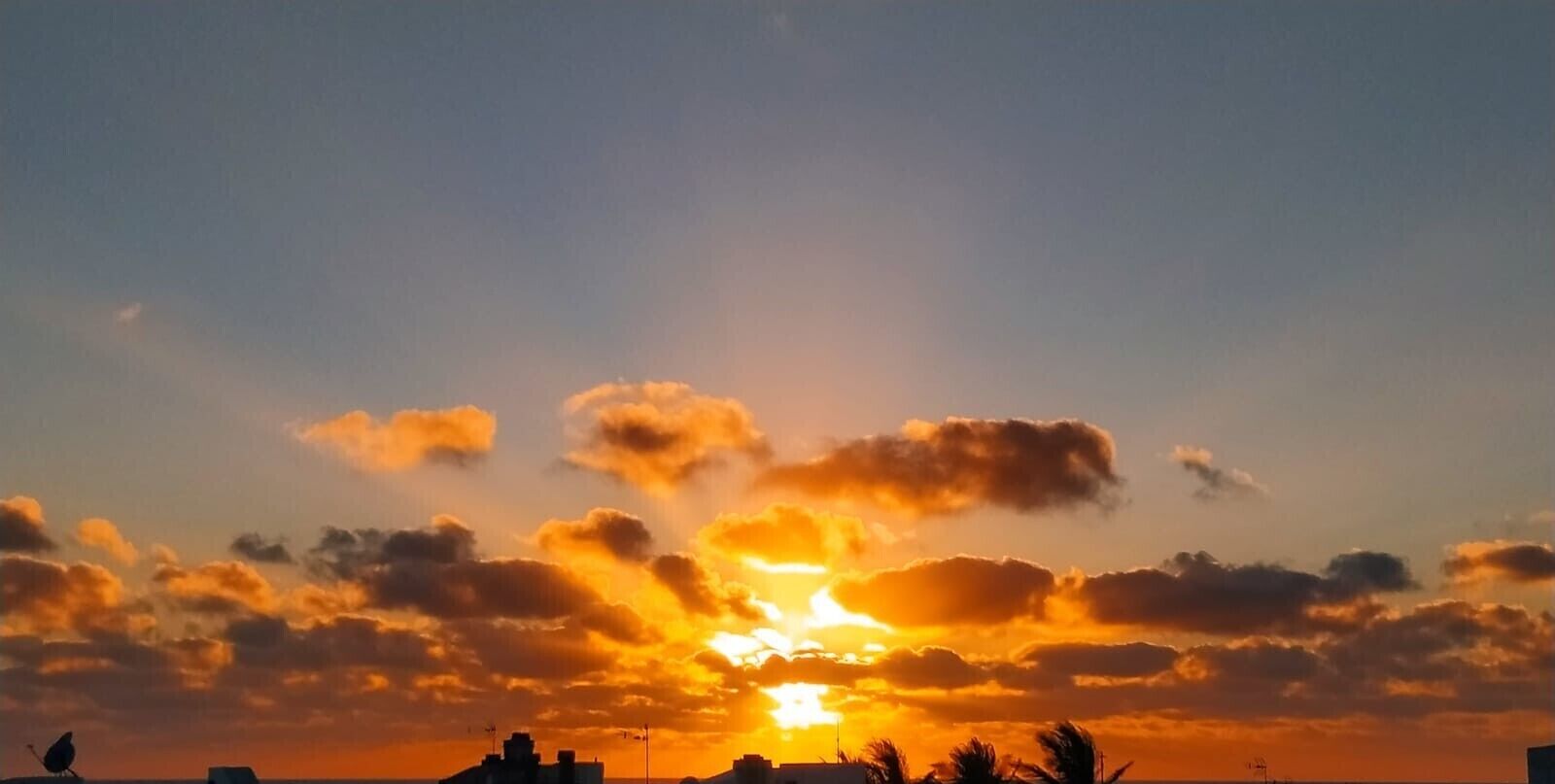 A sunset with clouds and silhouettes of buildings.