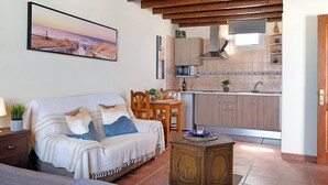 Una sala de estar acogedora con un sofá, una mesa de centro de madera y una cocina con armarios y un microondas.