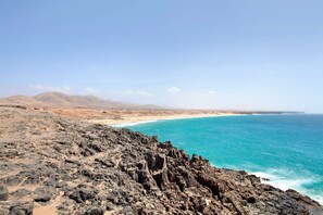 Une côte rocheuse avec une plage et des montagnes en arrière-plan.