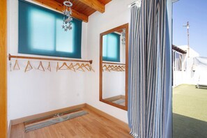 Quarto com piso de madeira, janela com cortina azul, espelho e cortina.